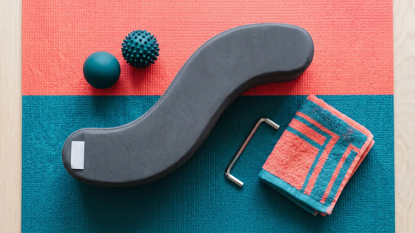 Curved grey lumbar bridge, massage balls, hex key and towel laid on a yoga mat